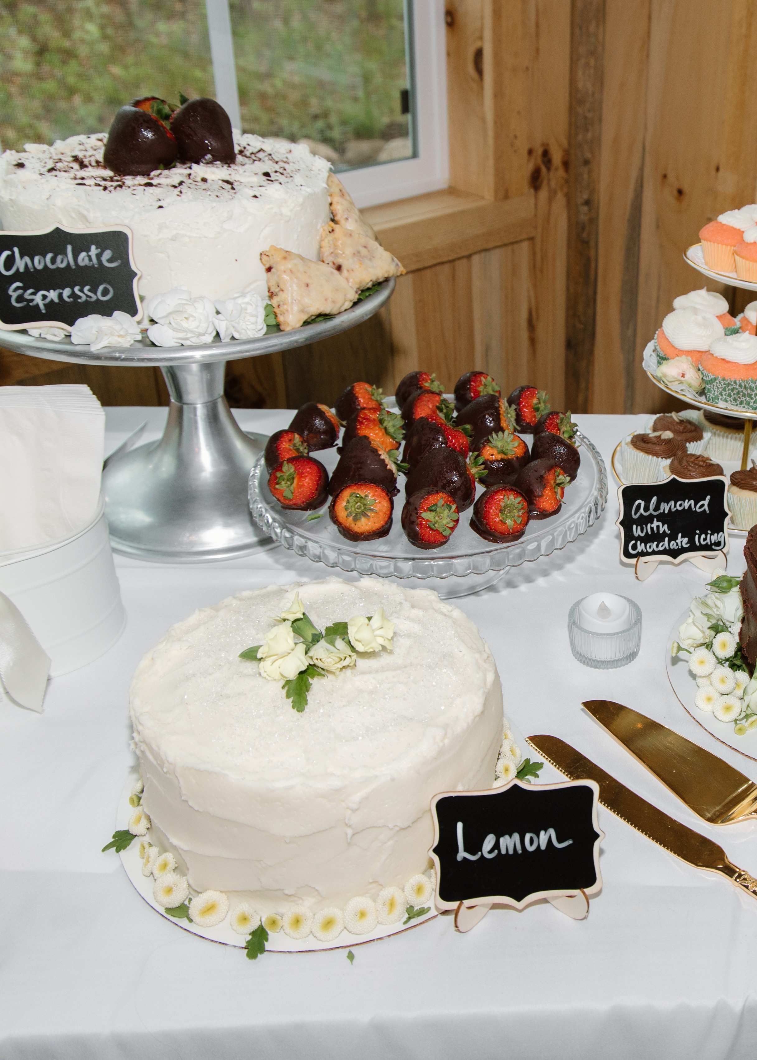 A bright Mother’s Day dessert table with cupcakes, cakes, flowers, and handwritten flavor signs