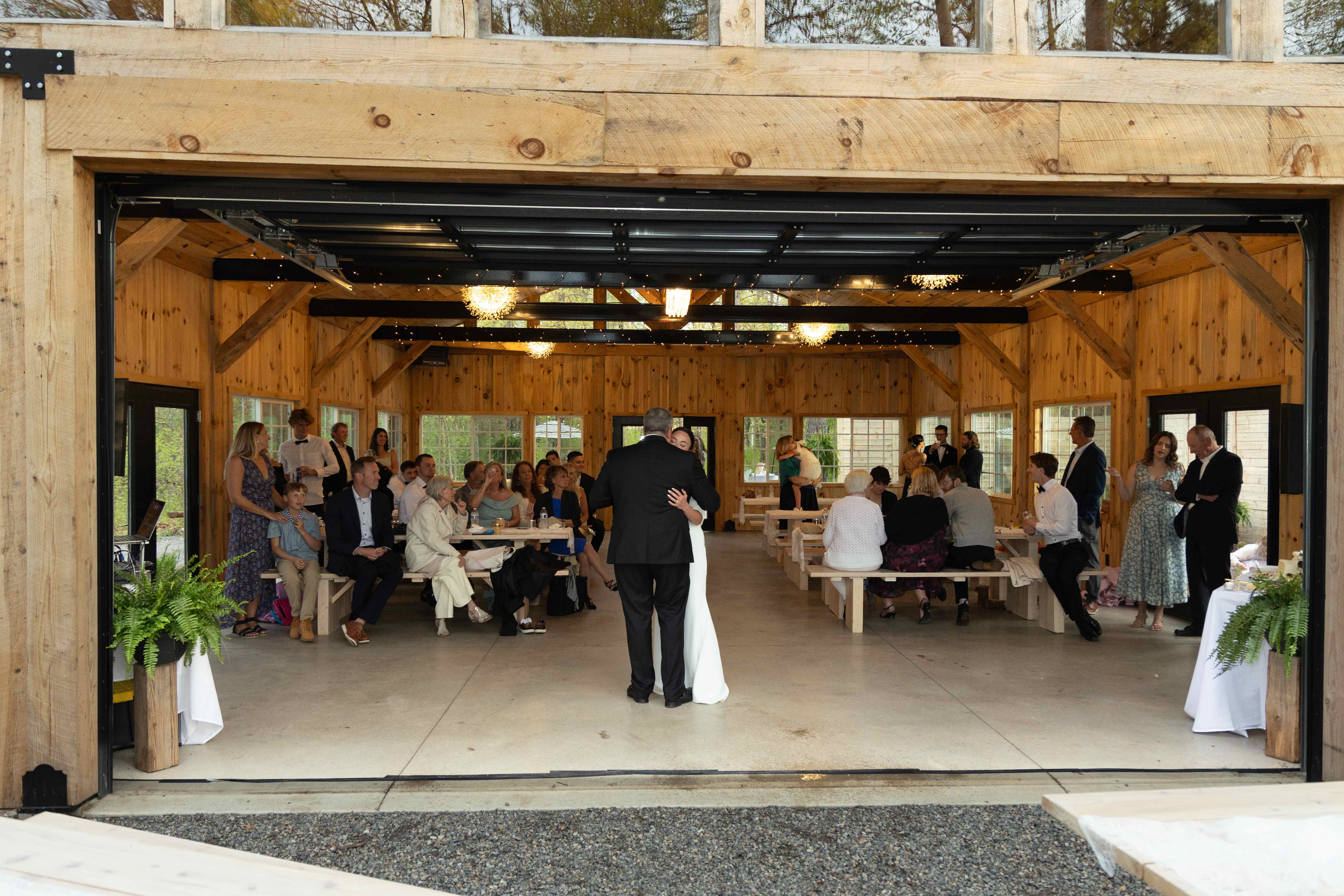 A couple sharing a first dance inside the barn with the glass garage door open to the forest