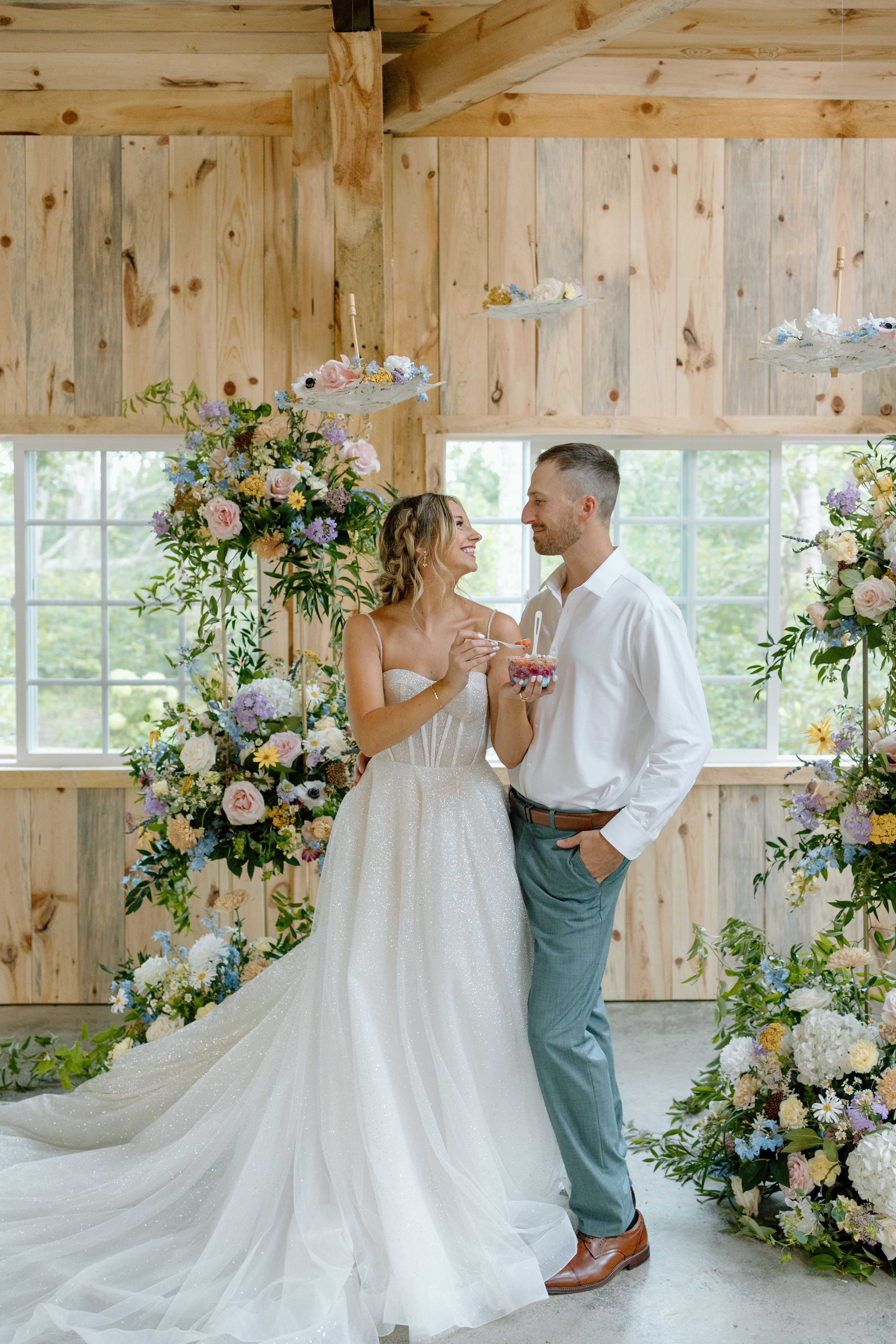 A couple beside towering pastel wildflower installations inside the Emerald Cottage barn by Celebrations Floral Design