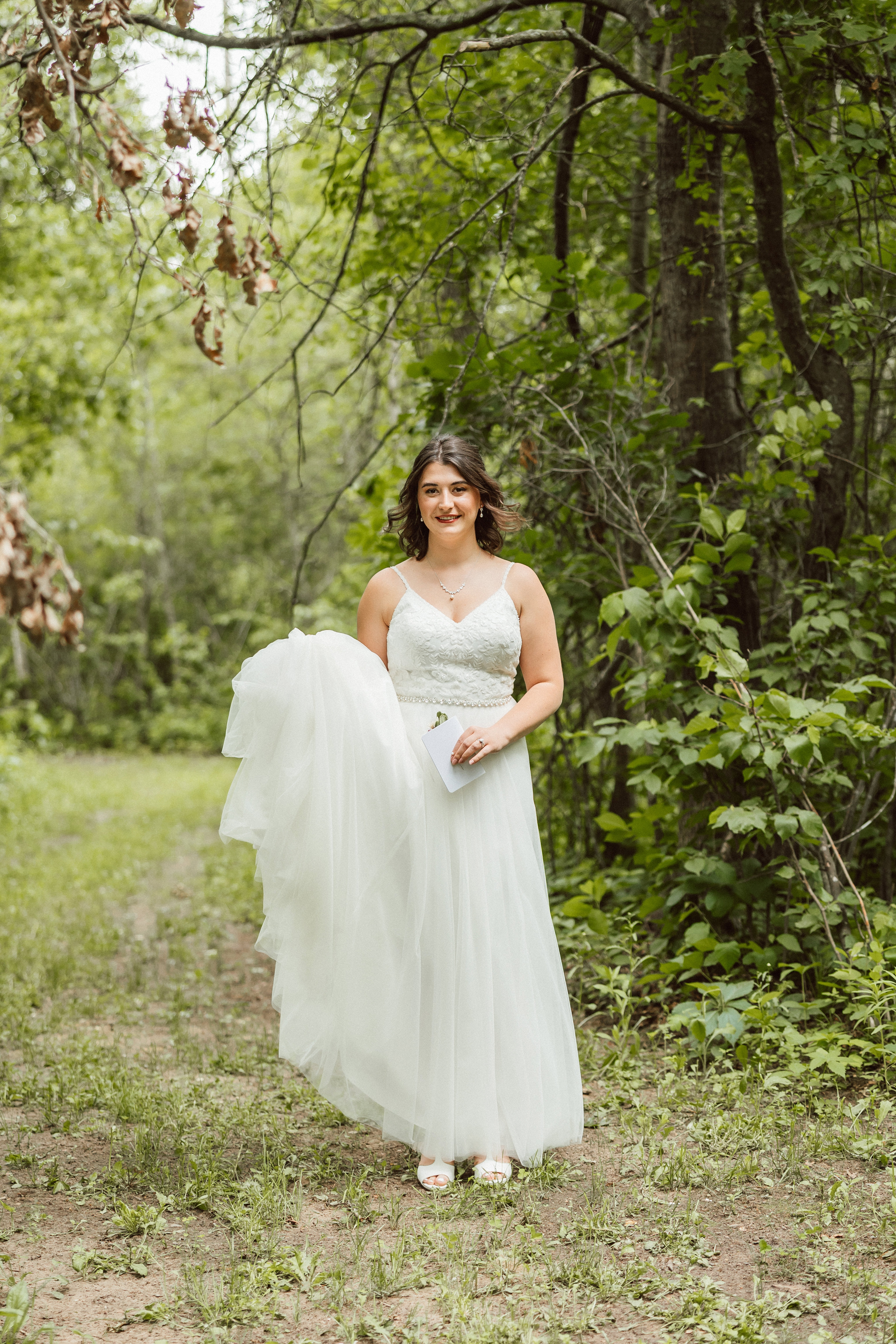 A bride on the wooded path at the Emerald Cottage holding her gown and vows, photographed by Rau Photo