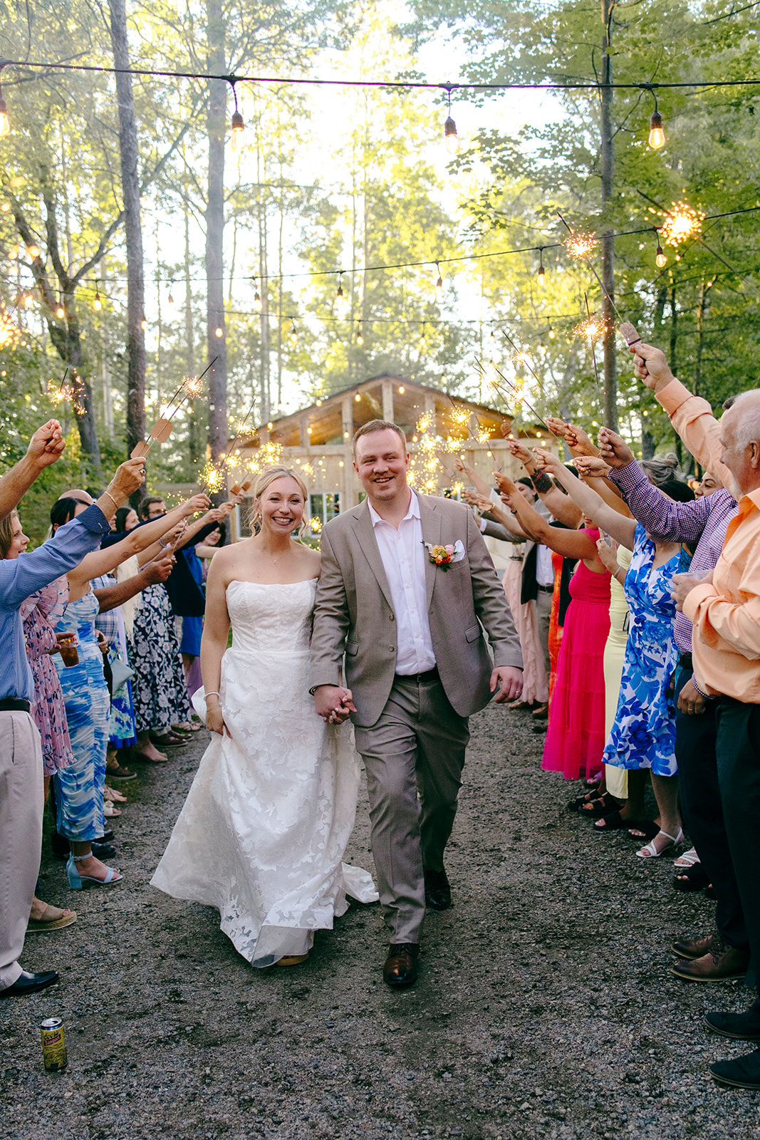 A bride and groom walking hand in hand through a tunnel of guests holding sparklers, the glowing cottage behind them at dusk