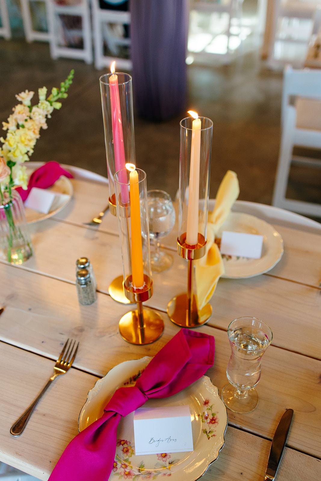 A candlelit place setting with taper candles, fuchsia and yellow napkins, and vintage floral china
