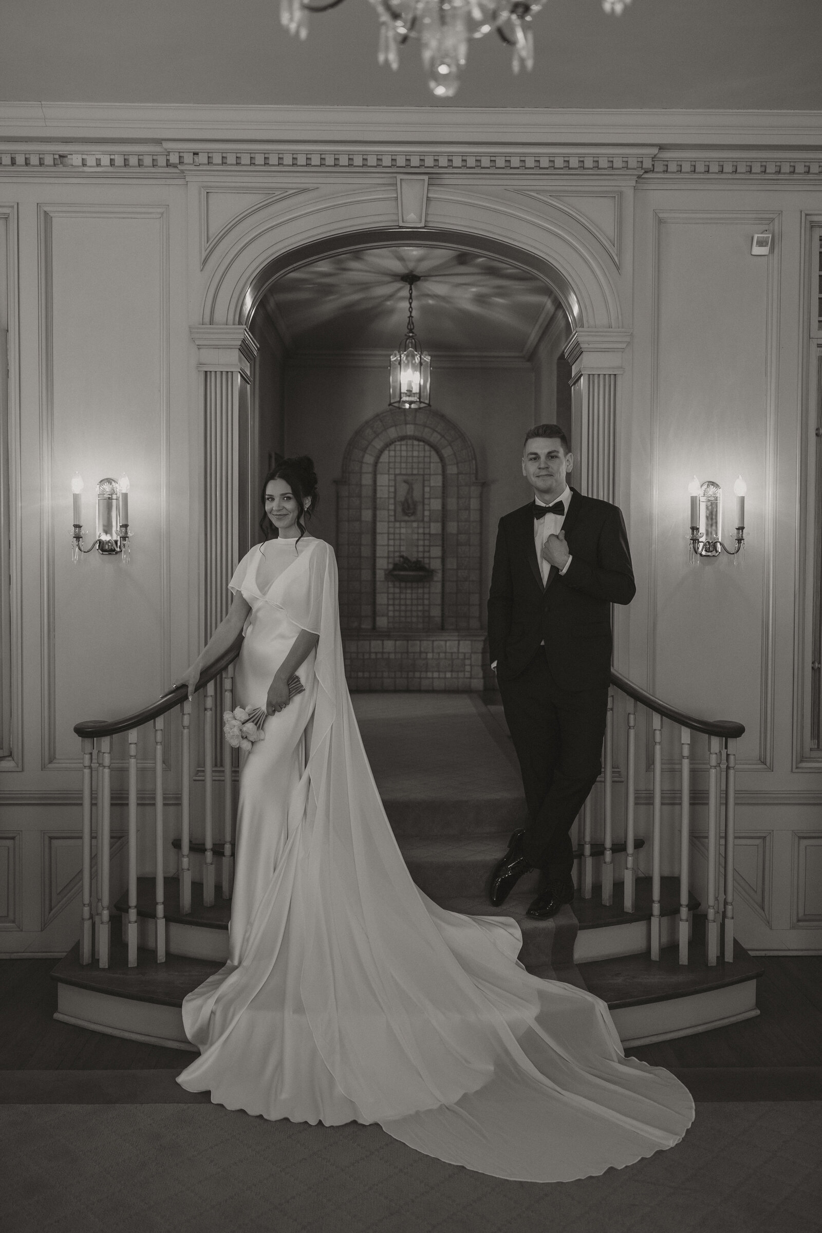 An elegant black-and-white portrait of a couple on a grand staircase, a film still by Precious Film Co